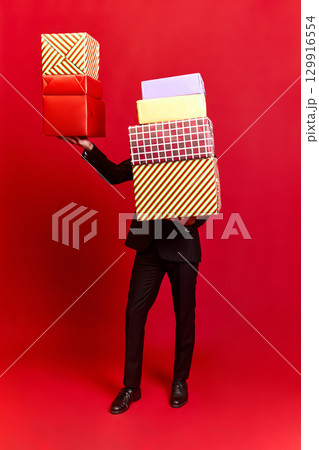 Person in black suit carrying colorful gift boxes on red background 129916554