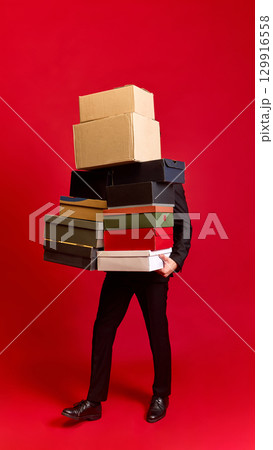 Person struggling to carry many stacked boxes on red background 129916558