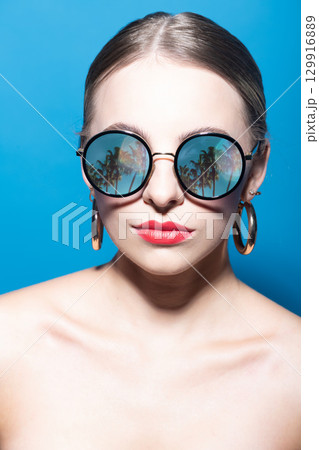Studio portrait of beautiful woman with red lipstick wearing sunglasses with palm trees reflection in it 129916889