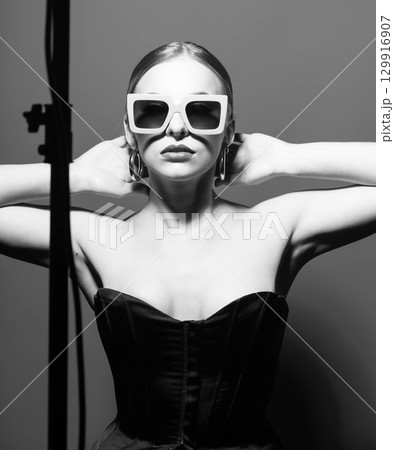 Woman portrait with classic hairstyle, retro sunglasses, lipstick, round earrings and black corset 129916907