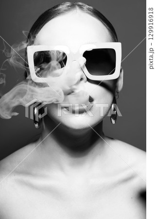Woman portrait with retro sunglasses and lipstick blowing white smoke from mouth Woman portrait with retro sunglasses and lipstick blowing white smoke from mouth 129916918