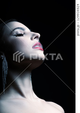 Woman studio portrait with fancy earrings, red lipstick and make-up blowing white smoke through mouth Woman studio portrait with fancy earrings, red lipstick and make-up blowing white smoke through mouth 129916924