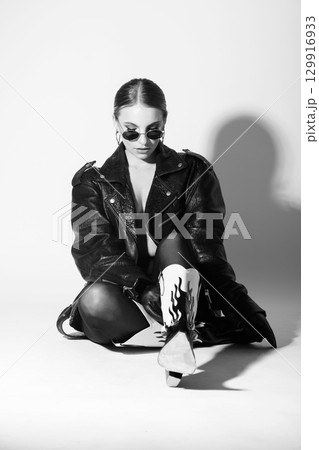 Woman studio portrait with black punk leather jacket, sunglasses and without bra Woman studio portrait with black punk leather jacket, sunglasses and without bra 129916933