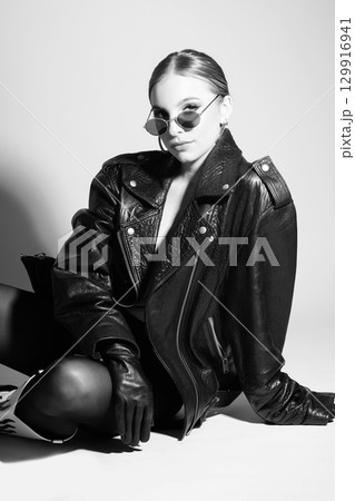 Woman studio portrait with black punk leather jacket, sunglasses and without bra 129916941