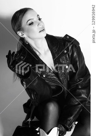 Woman studio portrait with black punk leather jacket and gloves looking aside camera 129916942