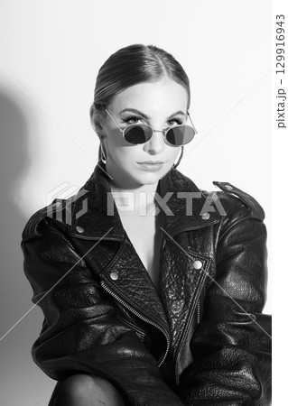 Woman black and white studio portrait with black punk leather jacket, sunglasses and without bra 129916943