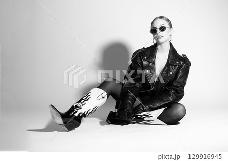 Woman black and white studio portrait with black punk leather jacket, sunglasses and without bra Woman black and white studio portrait with black punk leather jacket, sunglasses and without bra 129916945