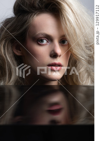 Beautiful woman with big wavy hair and black mirror reflection studio portrait 129917112