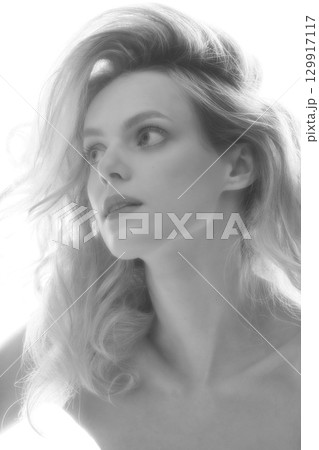 Beautiful woman with big wavy hair black and white studio portrait in bright background 129917117