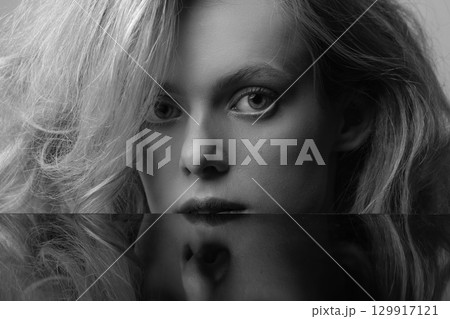 Beautiful woman with big wavy hair and black mirror reflection black and white studio portrait 129917121