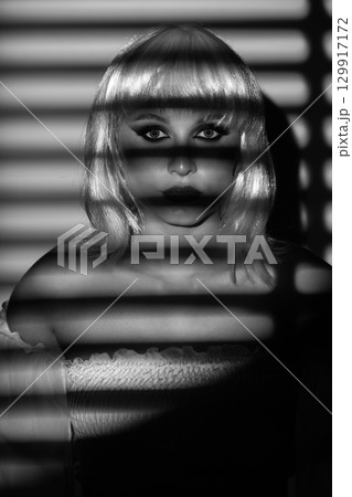 Beautiful woman with white wig illuminated by bright light through blinds Beautiful woman with white wig illuminated by bright light through blinds 129917172