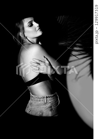 Black and white studio portrait of beautiful woman hugging herself and illuminated with bright studio light Black and white studio portrait of beautiful woman hugging herself and illuminated with bright studio light 129917319