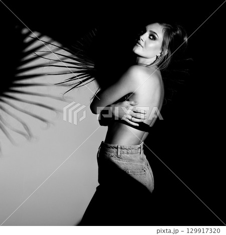 Black and white studio portrait of beautiful woman hugging herself and illuminated with bright studio light Black and white studio portrait of beautiful woman hugging herself and illuminated with bright studio light 129917320