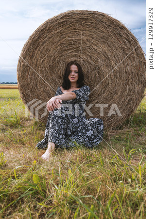 Woman Sitting by Hay Bale 129917329
