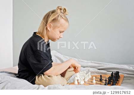 Cheerful little child girl playing chess while spending leisure time at home 129917652