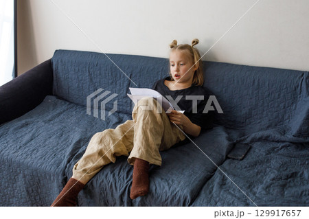 Funny little child girl reading book at home, indoor portrait 129917657