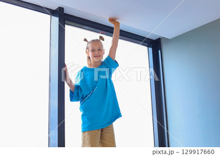 Adorable child standing high and touching the white ceiling with her hand at home. Adorable child standing high and touching the white ceiling with her hand at home. 129917660