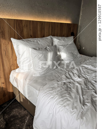 Close-up of a comfortable hotel bed with fluffy pillows and white sheets, illuminated by soft natural light. Ideal for themes of relaxation, travel, luxury, and comfort. High quality photo 129918587