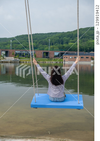 Person Relaxing on Swing by Scenic Lake Person Relaxing on Swing by Scenic Lake 129919412