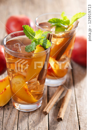 Refreshing peach iced tea in glass with ice cubes and cinnamon 129919713