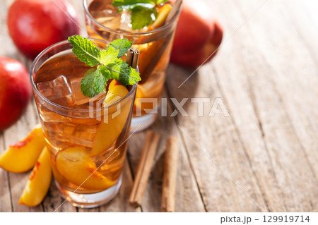 Refreshing peach iced tea in glass with ice cubes and cinnamon 129919714