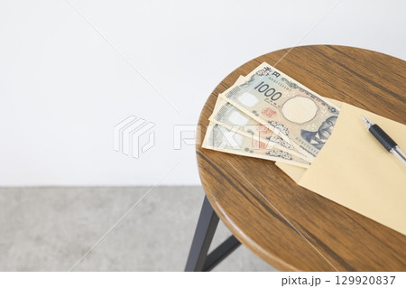 封筒と千円札三枚が木製テーブル上にある 封筒と千円札三枚が木製テーブル上にある 129920837