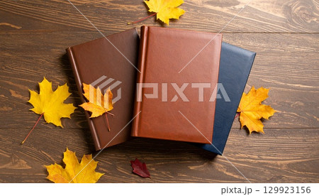 木のテーブルの上に置かれた3冊の本と秋の葉 129923156