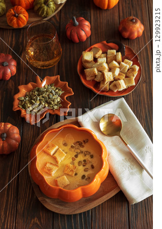 Creamy pumpkin soup with croutons and seeds, served in a pumpkin-shaped bowl on dark wooden table. Top view Creamy pumpkin soup with croutons and seeds, served in a pumpkin-shaped bowl on dark wooden table. Top view 129923215