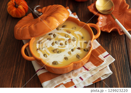 Autumnal lunch with pumpkin soup in a pumpkin-shaped bowl, croutons and festive decor on dark wooden table 129923220