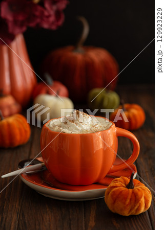 Cozy pumpkin latte in a pumpkin-shaped mug with whipped cream and spices, surrounded by autumn decor. Cozy pumpkin latte in a pumpkin-shaped mug with whipped cream and spices, surrounded by autumn decor. 129923229