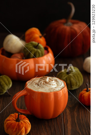 Cozy pumpkin latte in a pumpkin-shaped mug with whipped cream and spices, surrounded by autumn decor. 129923230