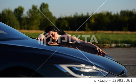 Beautiful smiling girl bought new electrical vehicle and hugging hood auto. Happy young woman enjoying modern electric automobile. Concept of buy or rent car. Slow motion Beautiful smiling girl bought new electrical vehicle and hugging hood auto. Happy young woman enjoying modern electric automobile. Concept of buy or rent car. Slow motion 129923361