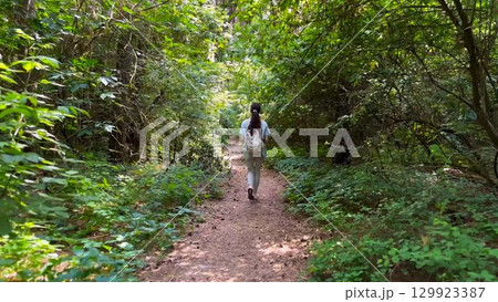 Young woman going along path at summer forest. Female with backpack walking among trail at wild nature. Unrecognizable girl enjoying stroll outdoor admiring beautiful scenic. Close up Rear view 129923387