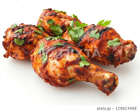 Succulent tandoori chicken legs, grilled to perfection, are displayed on a white background. They are garnished with fresh cilantro, highlighting the rich, vibrant color. 129923408