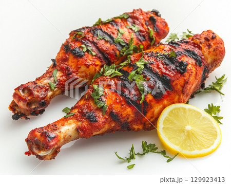 Succulent tandoori chicken legs, grilled to perfection, are displayed on a white background. They are garnished with fresh cilantro, highlighting the rich, vibrant color. 129923413