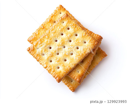 A close-up shot of a small pile of square creme crackers stacked against a plain white background. The crackers are golden-brown with small holes on their surface. A close-up shot of a small pile of square creme crackers stacked against a plain white background. The crackers are golden-brown with small holes on their surface. 129923993