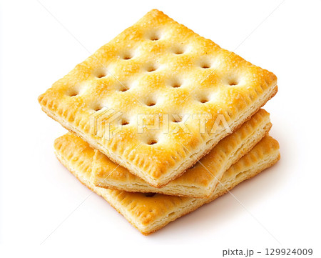 A close-up shot of a small pile of square creme crackers stacked against a plain white background. The crackers are golden-brown with small holes on their surface. 129924009