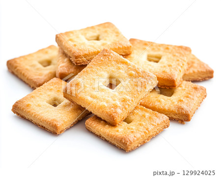 A close-up shot of a small pile of square creme crackers stacked against a plain white background. The crackers are golden-brown with small holes on their surface. A close-up shot of a small pile of square creme crackers stacked against a plain white background. The crackers are golden-brown with small holes on their surface. 129924025