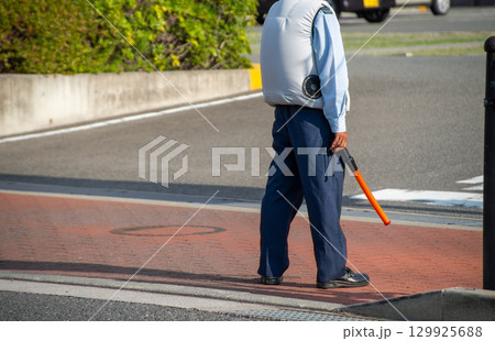 ファン付きウェアを着て駐車場の出口で待機している誘導員 129925688
