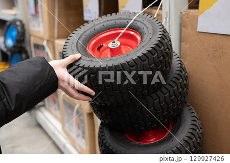 Individual examining multiple tires with red rims in a retail store during daytime hours Individual examining multiple tires with red rims in a retail store during daytime hours 129927426