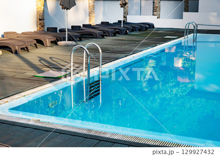 Outdoor swimming pool with metal ladder and lounge chairs around. 129927432