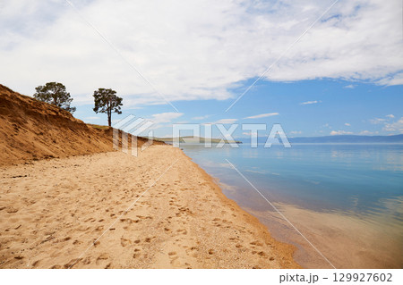 The shore of Lake Baikal on a cloudy summer day. Calm blue water, sandy beach. 129927602