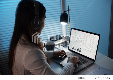 Young Asian women working late at night in dark room, using laptop.  129927883