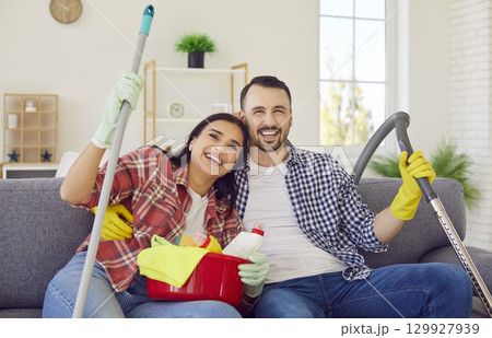 Happy couple with household cleaning supplies in hands sitting on sofa at home Happy couple with household cleaning supplies in hands sitting on sofa at home 129927939