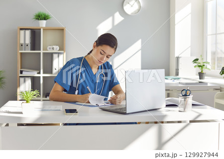 Woman Doctor Working at Desk with Laptop and Documents 129927944