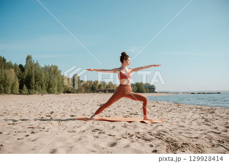 Young adult female practising yoga on a beach, Virabhadrasana II pose 129928414