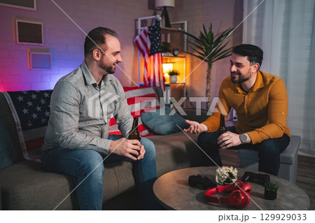 Two friends share stories and laughter over drinks in a cozy living room filled with warm ambiance and American decor 129929033