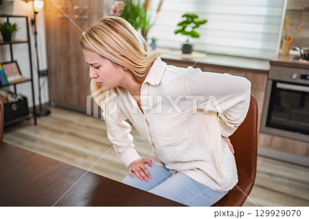 Struggling with discomfort while seated at a modern kitchen table 129929070