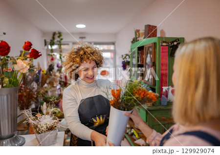 Cheerful florist shares vibrant flowers with a happy customer in a cozy shop 129929074