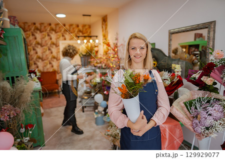 Flower shop vibrancy with cheerful florist showcasing bright blossoms in a cozy space Flower shop vibrancy with cheerful florist showcasing bright blossoms in a cozy space 129929077